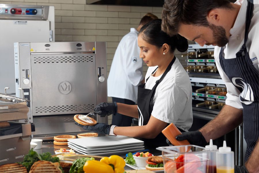 Female kitchen worker spreading sauce on a bun