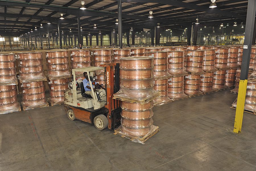 Worker on forklift moving pallets of copper pipe