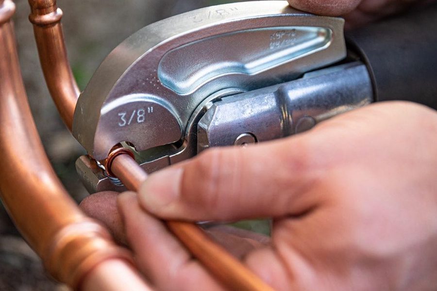 Closeup of hands holding a wrench working on copper pipe.